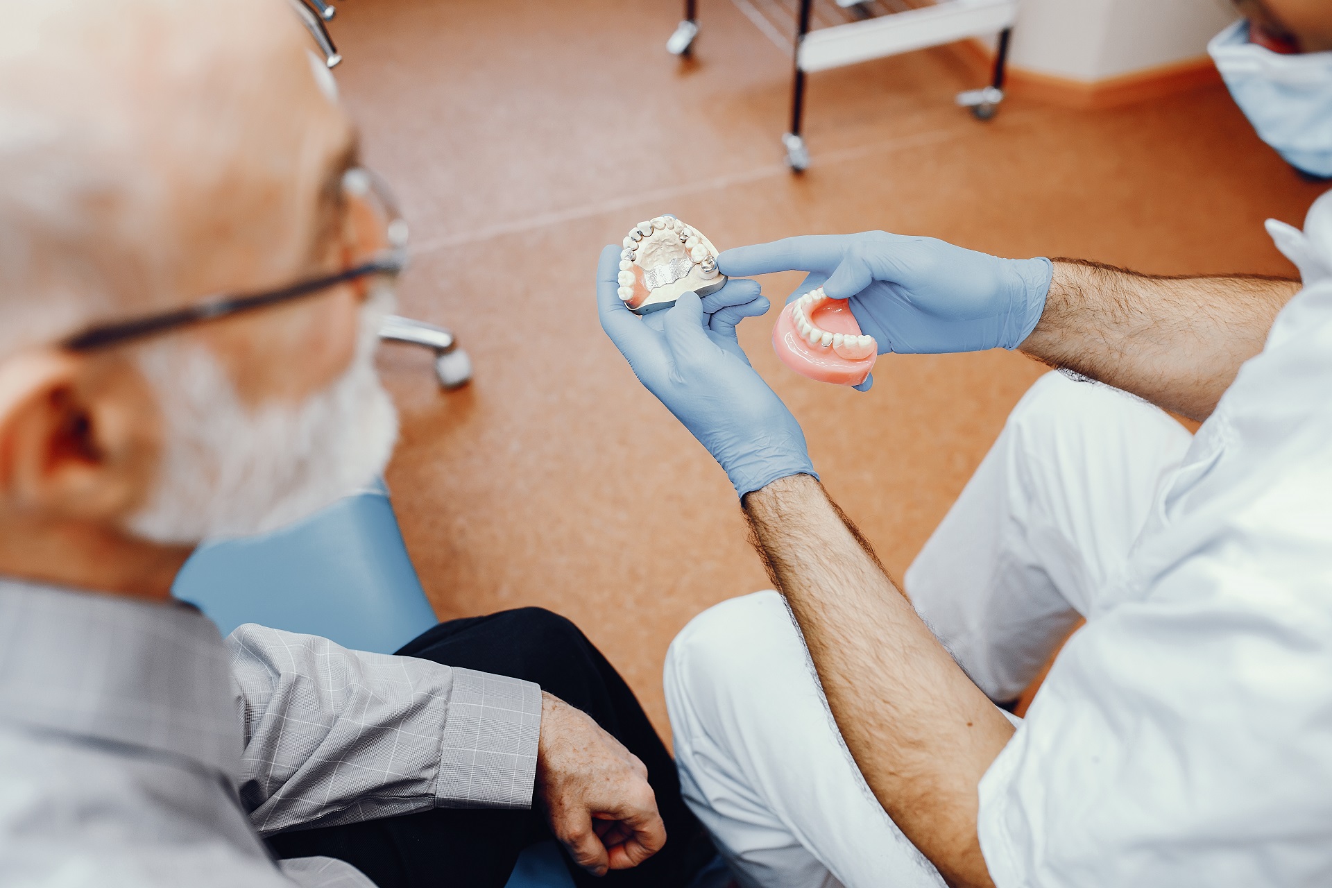 Older man watching a denturist repair a pair of dentures