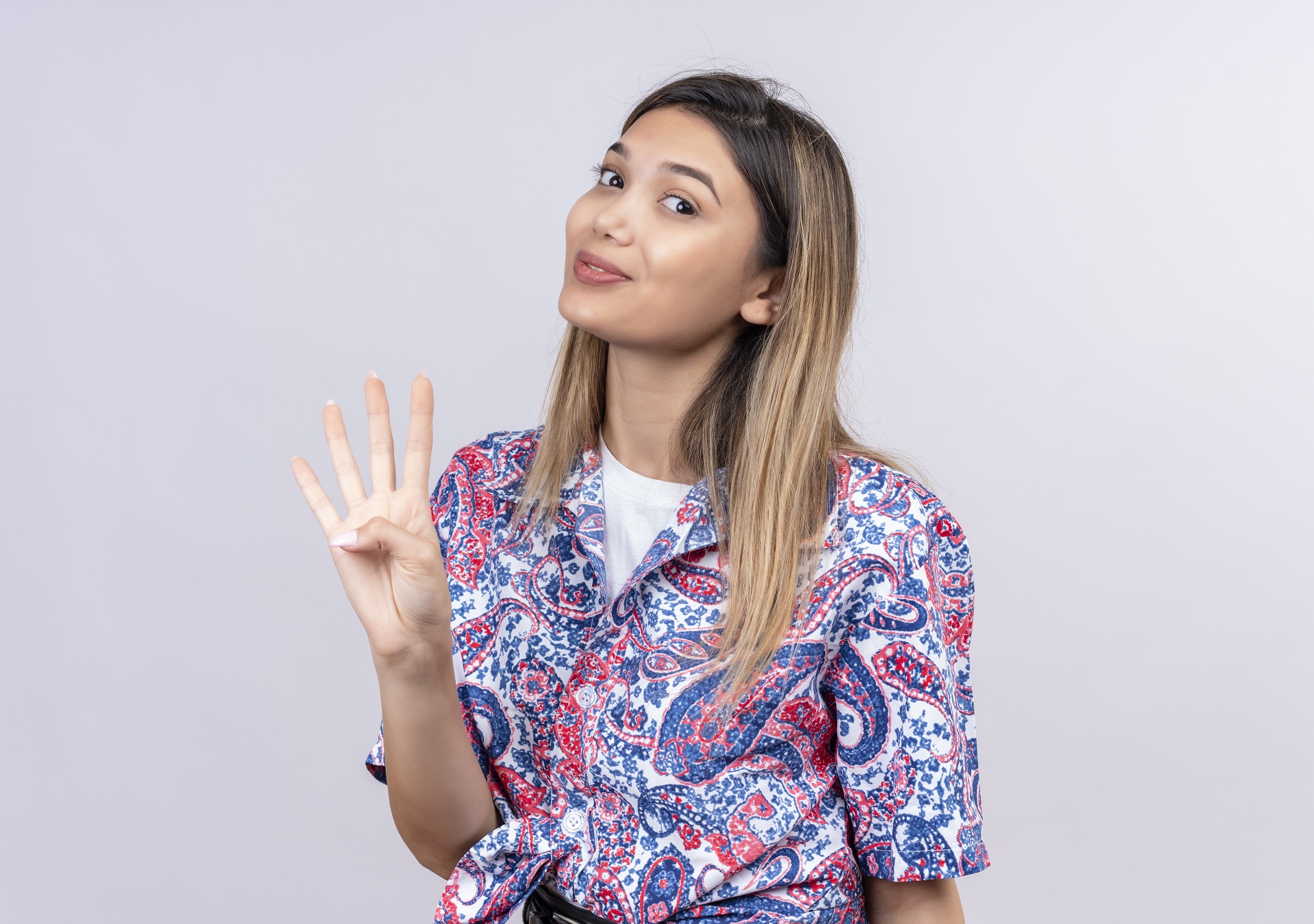 a beautiful young woman wearing paisley printed shirt showing number four with fingers while looking at the camera on a white background